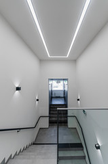 Clean white stairway staircase with glass railing in corridor in office building 