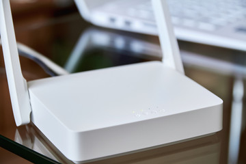 White wireless wi-fi router near a laptop on a glass table
