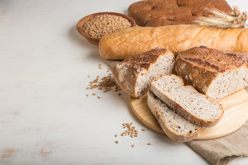 Sliced bread with different kinds of fresh baked bread on a white wooden background. side view, copy space.