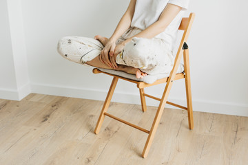 Girl sitting in lotus position on wooden chair in empty white room. Mental health. Copy space....