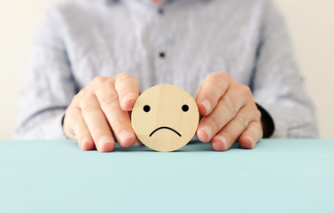male hand holding wooden circle with sad face. concept of anxiety, stress or sad emotions