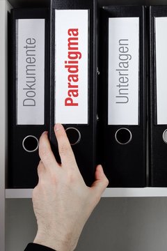 Paradigma &ndash; Finanzen/Statistik. Ordner im B&uuml;ro-Regal. Hand greift Unterlagen im Schrank. Beschriftung mit Wort
