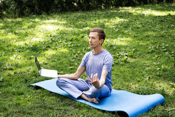 Young attractive white man learns to meditate in the park