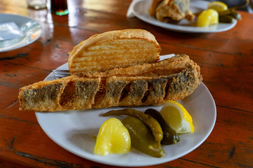 Balaton style hake ( balatoni hekk ) breaded deep fried fish at a restaurant with sour vegetables pickle and garlic bread toast a typical popular hungarian summer food