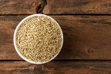 Dry rosemary leaves in bowl on rustic wooden table. Top view