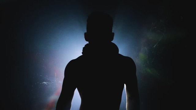 A young male dancer dancing in the dark against a light source. Sexy man with muscular body, elegance