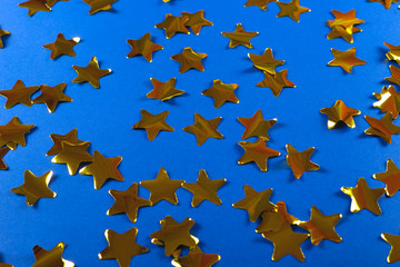 Gold shiny confetti in the shape of stars on a bright blue background. Festive and Christmas background. Top view, copy space
