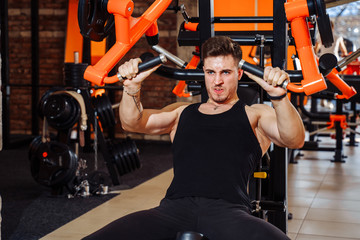 Fototapeta na wymiar Huge pressure. Half-length portrait of a young European brunette man doing gym with big tension. Strong muscular handsome attractive bodybuilder is a training workout