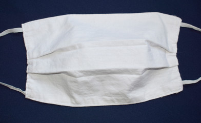 White protective face mask made of fabric on a dark background. Mask with elastic bands on the sides. View from above.