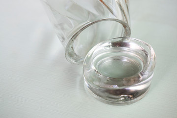 Broken glass cup on a white painted surface. Broken thick bottom of the glass.