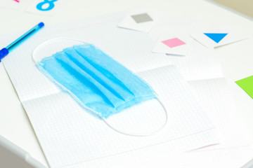 Medical mask over school notebook on withe desk. Home learning concept.