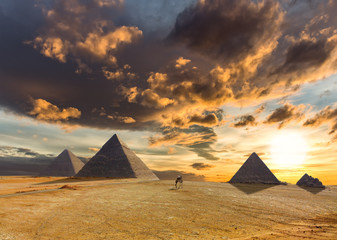 A dramatic sunrise with impressive clouds over the desert and pyramids at Giza in Egypt. A man in a...