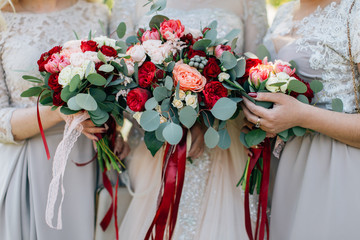 Bridesmaids holding bouquets closeup, marsala tapes. Roses and eucalyptus