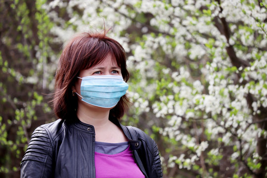 Woman in medical protective mask in a spring garden on cherry blossom background. Concept of quarantine during covid-19 coronavirus pandemic