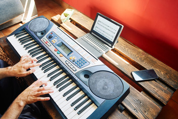 A man playing the piano at home while using a tablet to read the scores and the phone as a metronome