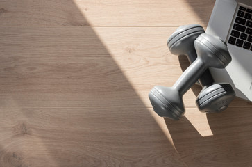 Online home training background with dumbbells, laptop and wooden surface