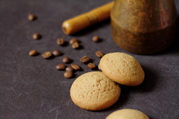 on a dark gray table is a jag for making coffee, a stirring stick, coffee beans, round cookies