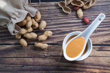 Peanut butter in a spoon and peanuts in wooden background. Healthy snack. Top view.