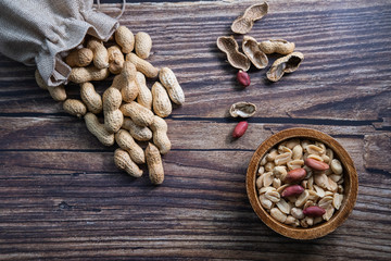 Peanuts in a wooden bowl and bag on wooden background. Raw and healthy snack. Top view.