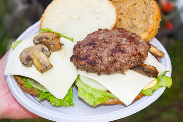 delicious hamburger made from buns, onions, green salad, cucumbers, cheese, beef, mushrooms and tomatoes on a white plate. international hamburger day concept