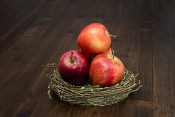 Ripe red apples in a wooden plate on the wooden table top made of boards with a dark textured surface.
