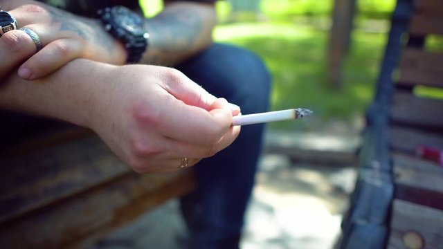A man smokes a cigarette. Male biker with tattoos and accessories. Smoking, harm to health. Smoking man in the park. 4k