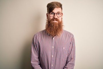 Handsome Irish redhead business man with beard wearing glasses over isolated background puffing cheeks with funny face. Mouth inflated with air, crazy expression.