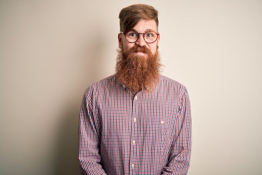 Handsome Irish redhead business man with beard wearing glasses over isolated background puffing cheeks with funny face. Mouth inflated with air, crazy expression.