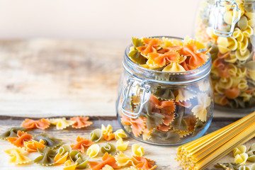Colored natural paste. Different types of italian pasta in glass jars on a yellow wooden table. copy space. Diet and nutrition concept.