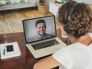 woman having a video conference call with a man on her laptop wearing a headset with notepad and mobile phone on the desk in her home office