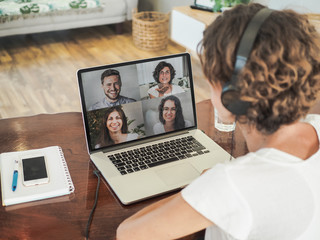 woman having a video conference call with four people at her laptop wearing a headset with notepad and mobile phone on the desk in her home office 