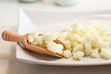 Milk kefir grains in wooden spoon with a glass of kefir in the back