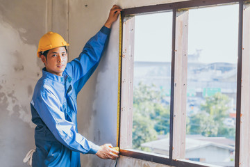 Worker measuring length window frame in construction site.