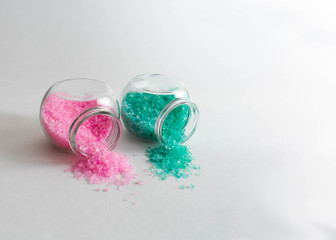 Jars with turquoise and light pink bath salts are on the left side of the frame. Horizontal photo. Objects on a white background. Banks are lie on its side. Bath salt spilled out into the background.