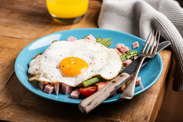 Healthy breakfast or lunch with fried egg, bread toast, green asparagus and tomatoes on blue plate on old wooden table