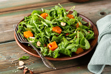 Paleo diet salad with arugula, baked pumpkin, hazelnut and sesame seeds on brown plate. Healthy food concept.