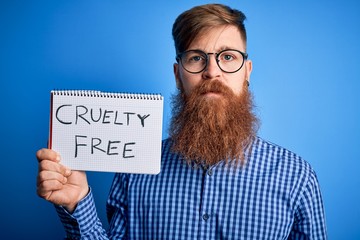 Redhead Irish man with beard holding cruelty free vegan cosmetics message over blue background with...