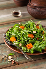 Autumn salad with arugula, baked pumpkin, hazelnut and sesame seeds on brown plate. Paleo diet food concept with copy space.