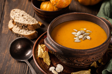 Home made pumpkin and carrot cream soup with seeds in old brown bowl. Healthy vegetarian food concept.