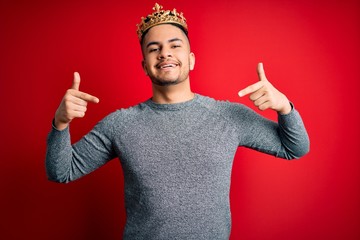 Young handsome man wearing golden crown of prince over isolated red background looking confident...