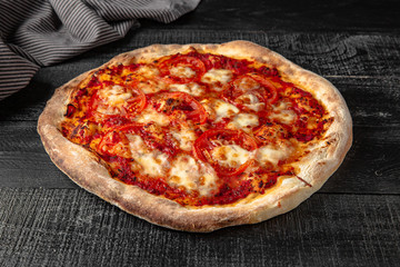 Tasty hot italian pizza with tomatoes and mozzarella on black wooden table. Pizzeria menu. Concept poster for Restaurants or pizzerias