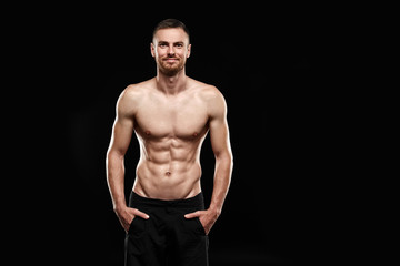 Fototapeta na wymiar Strong athletic man - athlete fitness model showing his perfect body isolated on black background with copyspace. Ectomorph bodybuilder with perfect abs, shoulders, biceps, triceps and chest.