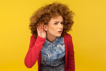 What are you saying? Portrait of woman with curly hair holding hand near ear and listening...