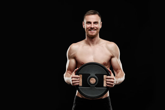 Strong athletic man - athlete fitness model showing his perfect body isolated on black background with copyspace. Ectomorph bodybuilder holding a black new barbell in his hands.