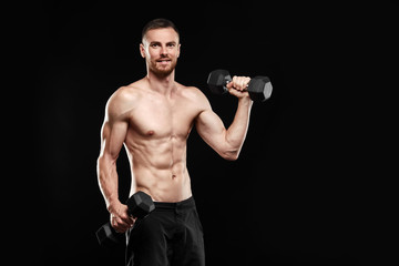 Fototapeta na wymiar Strong athletic man - crossfit athlete fitness model showing his perfect body isolated on black background with copyspace. Ectomorph bodybuilder holding a black new dumbbell in his hands.