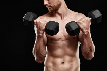 Fototapeta na wymiar Strong athletic man - athlete fitness model showing his perfect body isolated on black background with copyspace. Ectomorph bodybuilder holding a black new dumbbell in his hands close-up