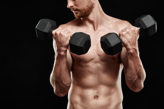Strong athletic man - athlete fitness model showing his perfect body isolated on black background with copyspace. Ectomorph bodybuilder holding a black new dumbbell in his hands close-up