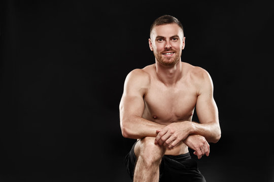 Strong smiling athletic man - athlete fitness model showing his perfect body isolated on black background with copyspace. After running, training, happy, got up on one knee close-up