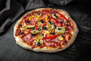 Tasty hot italian pizza with ham and vegetables on black wooden table. Pizzeria menu. Concept poster for Restaurants or pizzerias