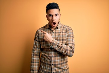Young handsome man wearing casual shirt standing over isolated yellow background Surprised pointing with finger to the side, open mouth amazed expression.